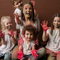 A happy group of children and woman covered in colorful powder, all smiles and joy.