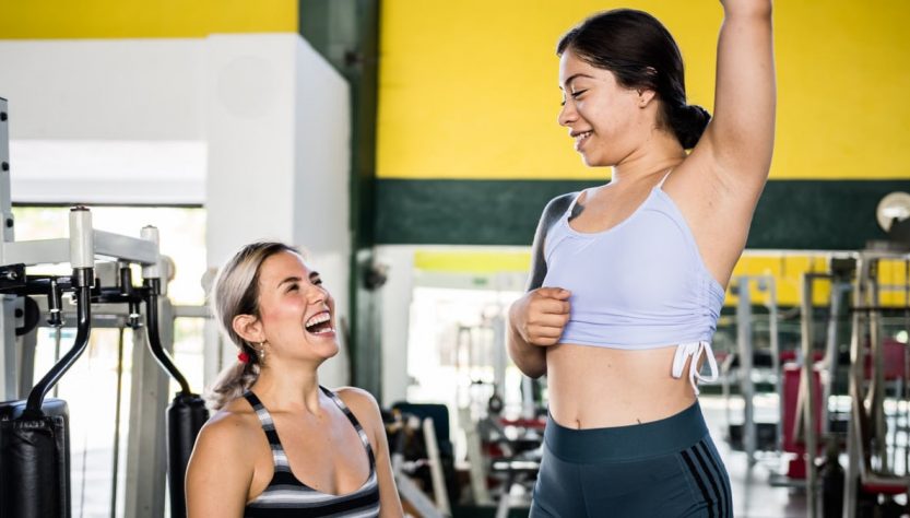 Two women in activewear sharing a joyful moment during a gym workout session.